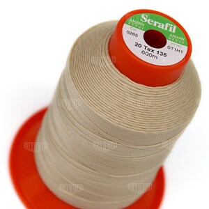 May include: A spool of beige thread labeled "Seratfil" by Amann Group. The label also includes the color number 0265, lot number ST1H1, and the thread specifications: 20 Tex 135, 600m.