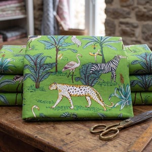 Könnte beinhalten: Ein Stapel grüner Stoffe mit Dschungel-Motiv, darunter ein Leopard, ein Zebra und ein Flamingo. Auf einem Holztisch liegen eine Schere und ein Lineal.
