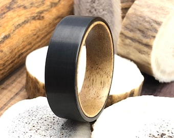 May include: A black tungsten carbide ring with a wood inlay. The ring is shown on a piece of antler.