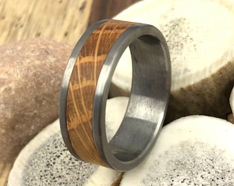 May include: A silver and wood ring with a wood grain pattern. The ring is sitting on a white surface.