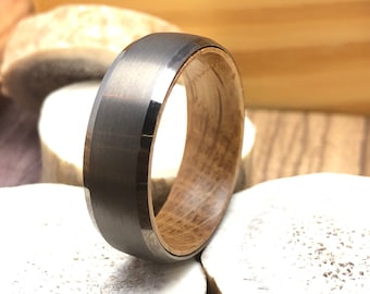 May include: A black tungsten carbide ring with a beveled edge and a wood inlay. The ring is on a white background.