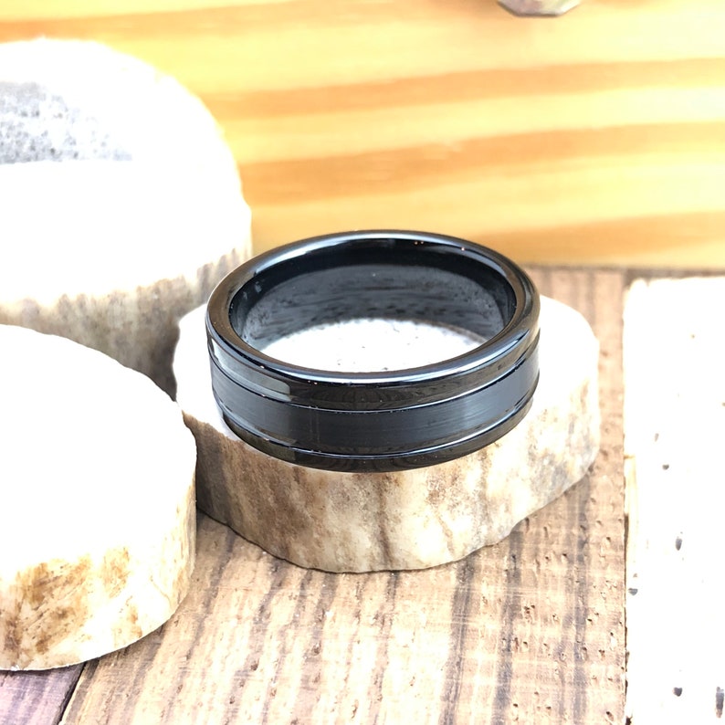 Op de afbeelding: Een zwarte keramische ring met een geborstelde afwerking en een zwarte inlay. De ring ligt op een stuk hout.