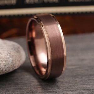 May include: A rose gold tungsten carbide ring with a brushed finish and a thin rose gold band.
