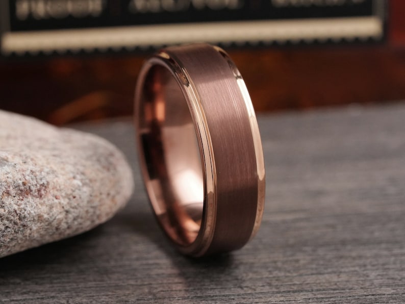 May include: A rose gold tungsten carbide ring with a brushed finish and a thin rose gold band.
