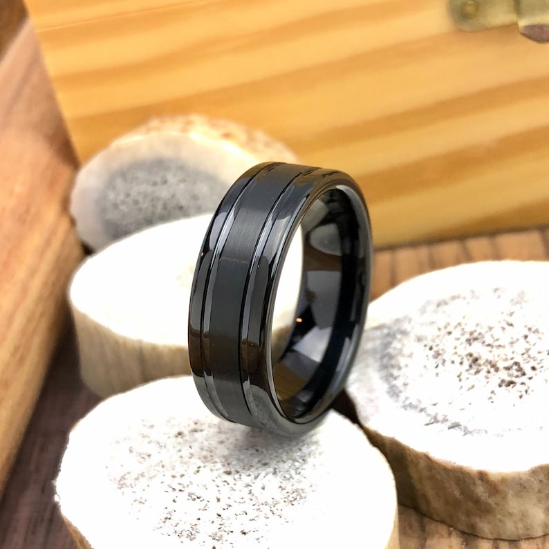 Op de afbeelding: Een zwarte ring van wolfraamcarbide met een geborstelde afwerking en twee groeven rond de band.