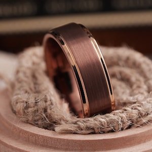 May include: A rose gold tungsten carbide ring with a brushed finish and a polished beveled edge.