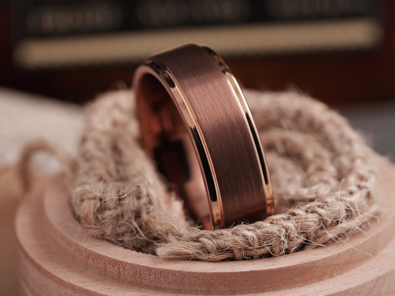 May include: A rose gold tungsten carbide ring with a brushed finish and a polished beveled edge.