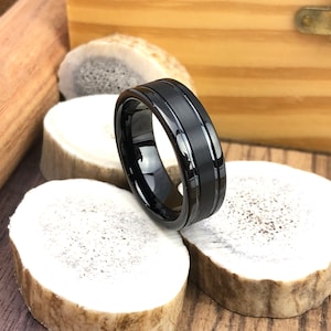 Op de afbeelding: Een zwarte ring van wolfraamcarbide met twee gepolijste groeven. De ring heeft een geborstelde afwerking.