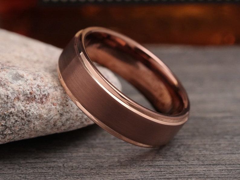 May include: A rose gold tungsten carbide ring with a brushed finish and a polished edge.