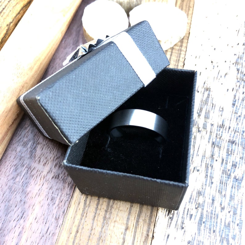 Op de afbeelding: Een zwarte ring in een zwarte fluwelen ringdoos met een wit lint.