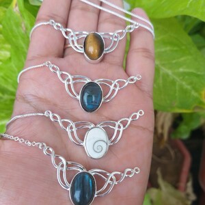 May include: Four silver necklaces with different oval-shaped gemstones. The necklaces feature a Celtic knot design. The gemstones are tiger's eye, labradorite, a white shell with a spiral pattern, and blue labradorite.