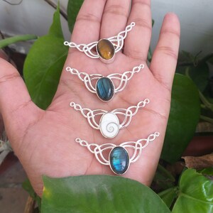 May include: Four silver Celtic knot pendant necklace connectors with different gemstone cabochons. The stones are a brown tiger's eye, a blue labradorite, a white abalone shell, and a blue labradorite.