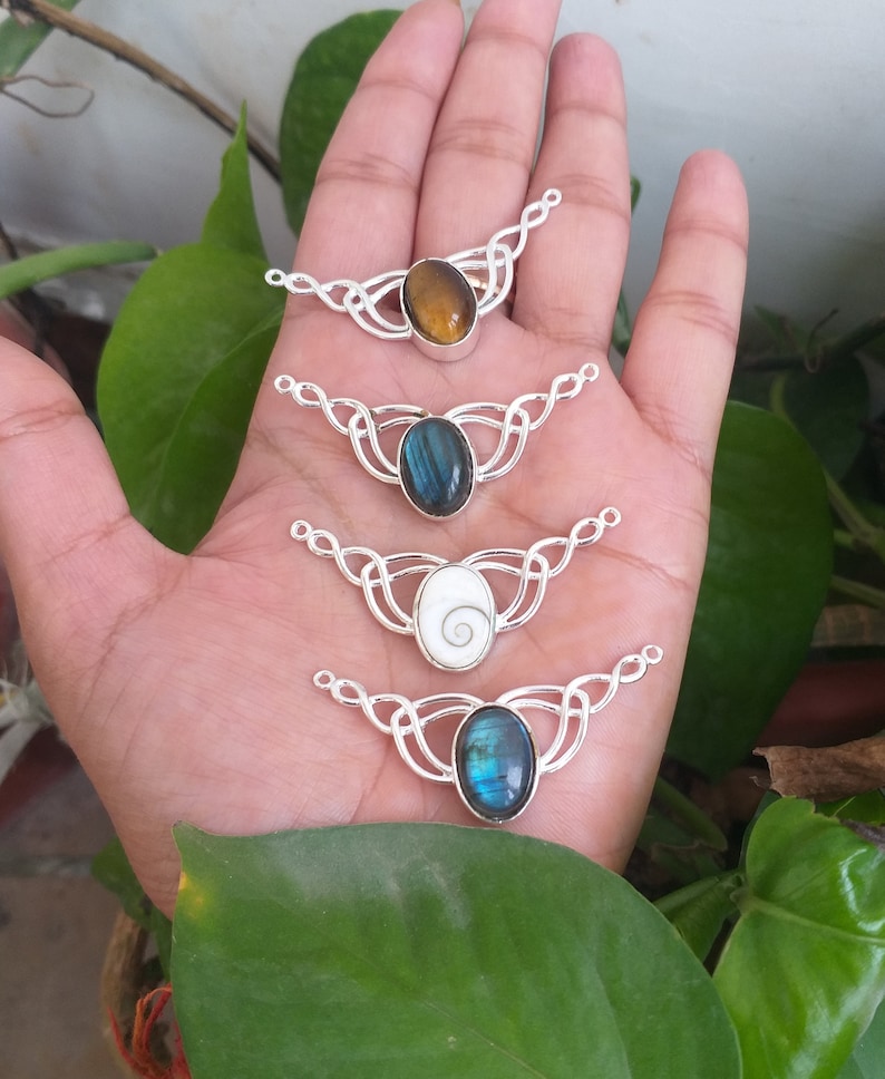 May include: Four silver Celtic knot pendant necklace connectors with different gemstone cabochons. The stones are a brown tiger's eye, a blue labradorite, a white abalone shell, and a blue labradorite.