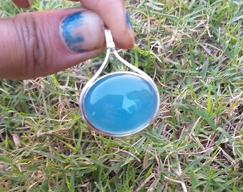 May include: A silver pendant featuring a round, light blue gemstone. The pendant is suspended from a silver chain.