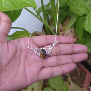 May include: A silver necklace with a brown tiger's eye gemstone pendant. The pendant is set in a Celtic knot design.