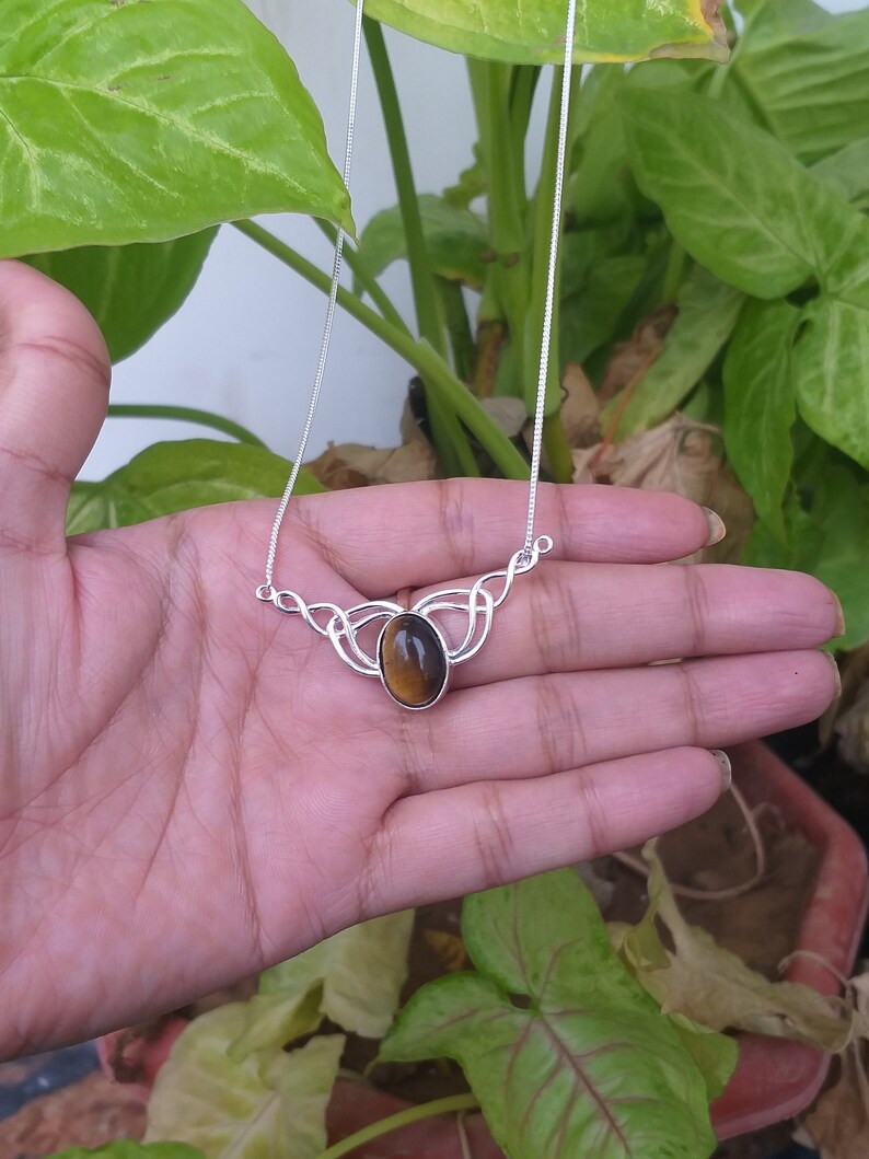 May include: A silver necklace with a brown tiger's eye gemstone pendant. The pendant is set in a Celtic knot design.