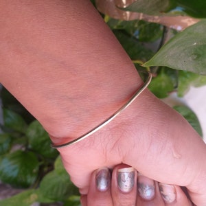 May include: A simple gold bangle bracelet on a person's wrist.