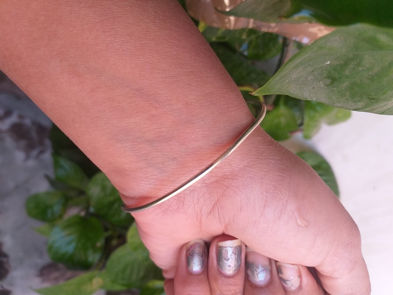 May include: A simple gold bangle bracelet on a person's wrist.