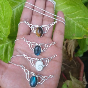 May include: Four silver necklaces with different gemstone pendants. The pendants are oval shaped and feature a tiger's eye, labradorite, a white shell, and another labradorite.