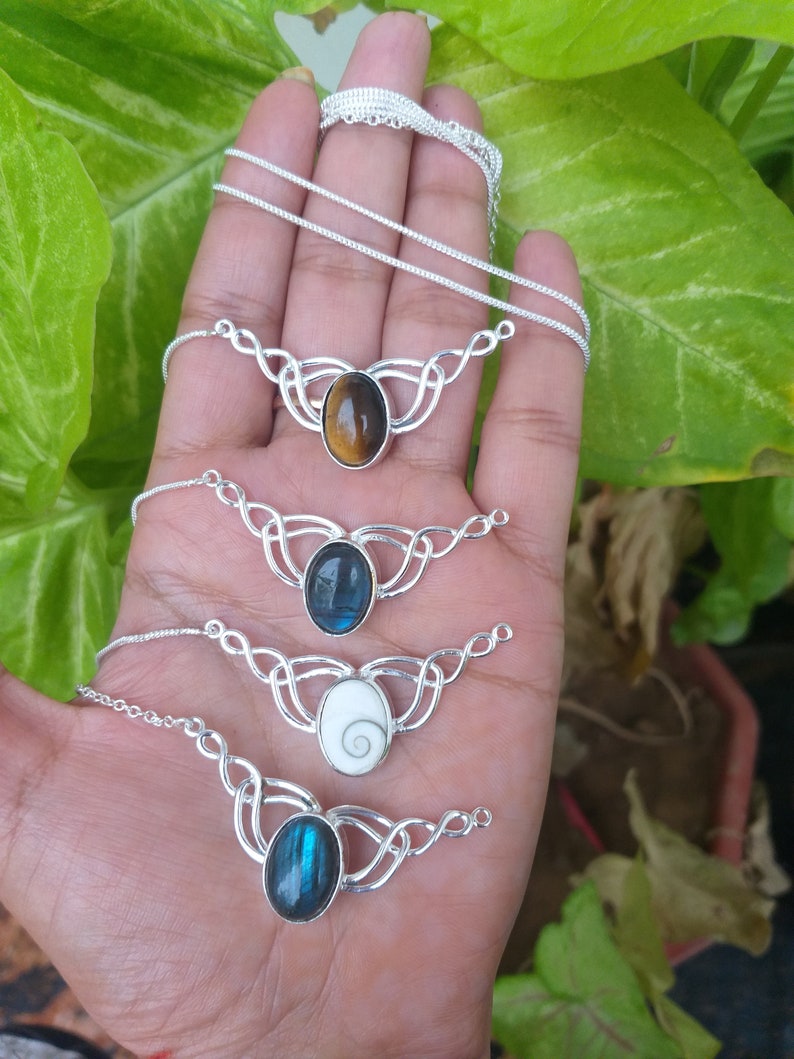 May include: Four silver necklaces with different gemstone pendants. The pendants are oval shaped and feature a tiger's eye, labradorite, a white shell, and another labradorite.