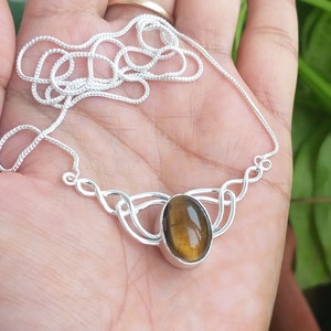 May include: A silver necklace with a brown and gold tiger's eye stone pendant. The pendant is set in a silver Celtic knot design.