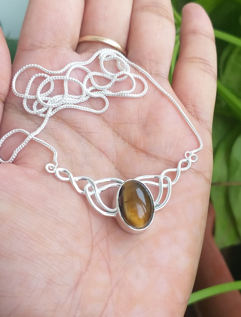 May include: A silver necklace with a brown and gold tiger's eye stone pendant. The pendant is set in a silver Celtic knot design.