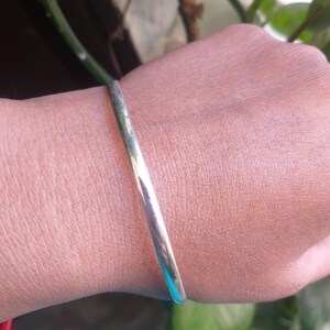 May include: A silver bangle bracelet on a person's wrist.
