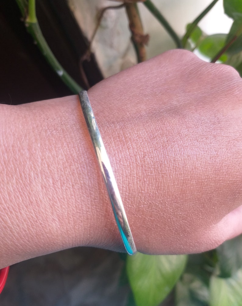 May include: A silver bangle bracelet on a person's wrist.