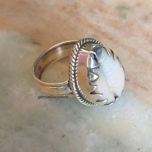 May include: A silver ring with a white shell set in a silver bezel. The ring has a rope-like design around the bezel.
