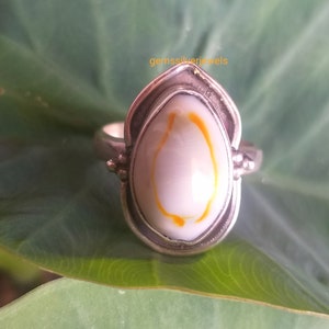 K&ouml;nnte beinhalten: Ein silberner Ring mit einer wei&szlig;en und orangefarbenen Muscheleinlage. Der Ring hat eine Tropfenform und ist in eine silberne Band gefasst.