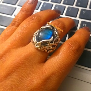 Puede incluir: Un anillo de plata con una piedra preciosa azul engastada en un diseño detallado y ornamentado. El anillo se lleva en un dedo.