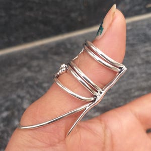 Può includere: Un anello da dito color argento dal design unico. L'anello presenta più fasce ed elementi decorativi, creando un accessorio intricato e accattivante. L'anello è progettato per coprire una parte del dito.