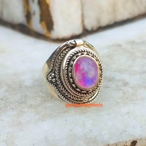 May include: A silver ring with an oval-shaped pink opal gemstone set in a decorative silver bezel. The ring has a detailed design with intricate silverwork.