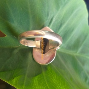 K&ouml;nnte beinhalten: Ein silberner Ring mit einem dunkelgr&uuml;nen Edelstein, der in eine silberne Fassung gefasst ist. Der Ring liegt auf einem gr&uuml;nen Blatt.