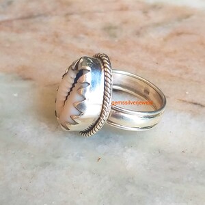 May include: A silver ring with a white shell inlay. The ring has a rope-like design on the band and a scalloped edge around the shell.