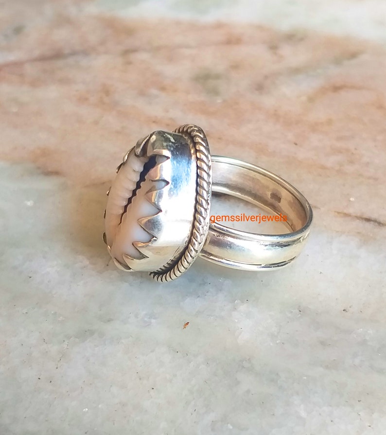 May include: A silver ring with a white shell inlay. The ring has a rope-like design on the band and a scalloped edge around the shell.