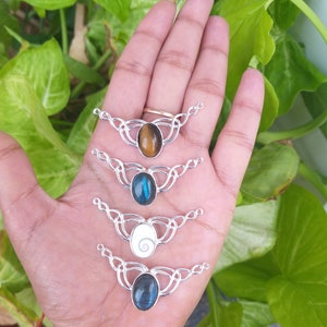 May include: Four silver pendant necklaces with different gemstone cabochons. The pendants feature a Celtic knot design. The gemstones are tiger's eye, blue labradorite, white mother of pearl, and blue labradorite.