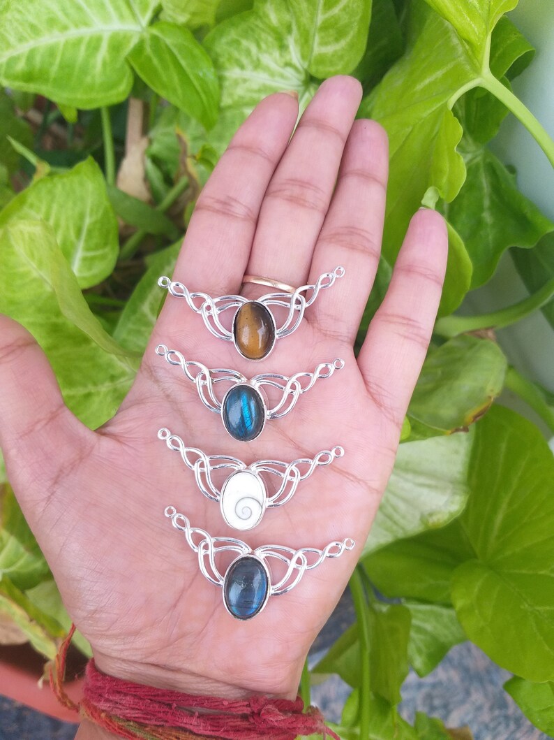 May include: Four silver pendant necklaces with different gemstone cabochons. The pendants feature a Celtic knot design. The gemstones are tiger's eye, blue labradorite, white mother of pearl, and blue labradorite.