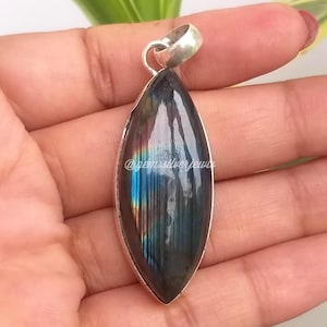 May include: A marquise-shaped pendant with a polished, iridescent labradorite stone set in a silver bezel. The stone displays flashes of blue, green, and gold. The pendant has a silver loop for a chain.