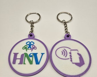 May include: Two circular keychains with purple borders and white centers. The left keychain features the text HNV in purple, green, and blue, with three small scissor icons above. The right keychain displays a purple icon of a hand holding a phone.