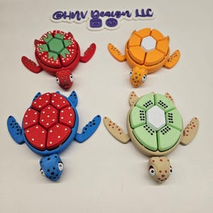 May include: Four colourful turtle puzzle toys. Each turtle has a different coloured shell with a unique pattern. The shells are made of multiple pieces that can be rearranged. The turtles are made of plastic and have a 3D printed look.