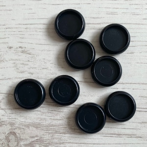 May include: Eight black round furniture pads on a white wood surface.