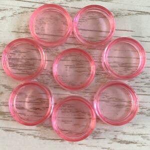 May include: Nine pink plastic rings, each with a smooth, round interior. The rings are arranged in a circular pattern on a light wood surface.