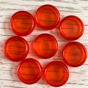 May include: Eight orange plastic game pieces, possibly for a board game, arranged in a circle on a light wood surface.