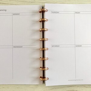 May include: A white weekly planner with a black and white grid layout. The planner has a section for notes, Monday through Sunday, and a space for the week commencing date. The planner is bound with a gold metal coil.