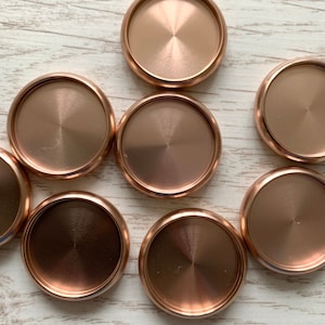 May include: Seven round, metallic, rose gold coloured coasters. The coasters have a smooth, shiny surface.