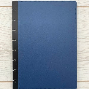 A blue faux leather Discbound planner cover, slightly larger than A5 sized paper, with black polypropylene mushroom hole punched edges