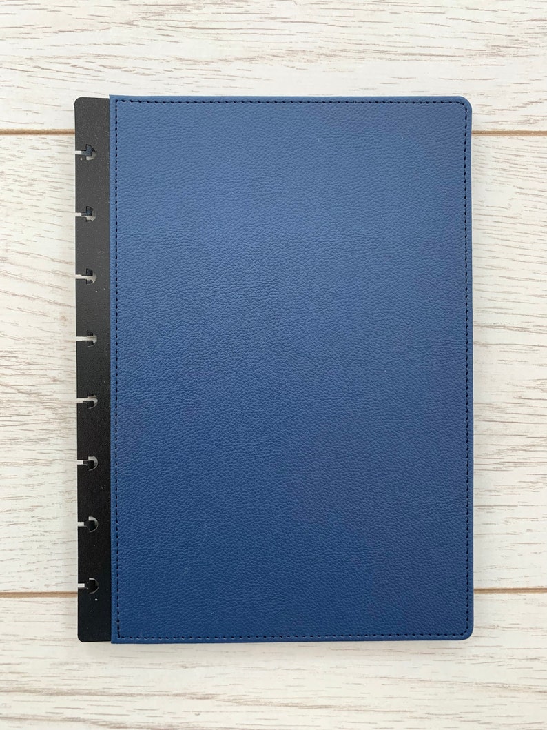 A blue faux leather Discbound planner cover, slightly larger than A5 sized paper, with black polypropylene mushroom hole punched edges