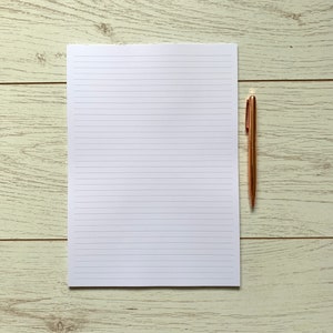 May include: A white lined notepad with a gold pen on a light wood surface.