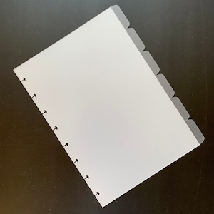 以下が含まれることがあります： 透明なプラスチックカバーとタブが付いた白いノート。ノートはリングバインディングシステムを採用しており、紙の整理と保管に適しています。